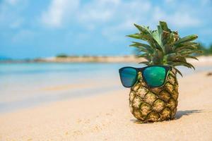 Ananas mit Sonnenbrille auf tropischem Strandhintergrund. Sommerkonzept