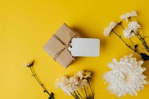 Geschenkbox mit leerem Etikett und Blumen wird auf gelbem Hintergrund platziert foto