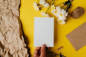 eine leere Karte mit Umschlag und Blume wird auf gelben Hintergrund gelegt foto