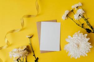 eine leere Karte mit Umschlag und Blumen wird auf gelben Hintergrund gelegt foto