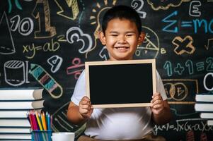 Kind sitzt und hält Tafel im Klassenzimmer foto