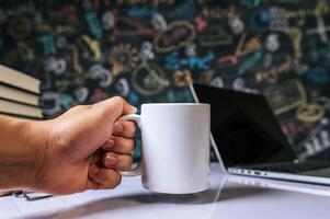 die Hand hob die Tasse auf dem Tisch im Klassenzimmer auf. foto