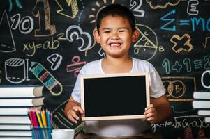 Kind sitzt und hält Tafel im Klassenzimmer foto