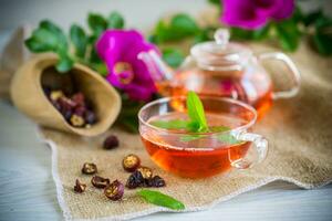 gebraut Hagebutte Tee im ein Glas Teekanne mit Hagebutte Blumen und Minze foto