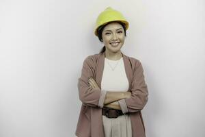 ein zuversichtlich lächelnd asiatisch Frau Mitarbeiter tragen Sicherheit Helm Stehen mit Waffen gefaltet und suchen beim das Kamera isoliert Über Weiß Hintergrund foto