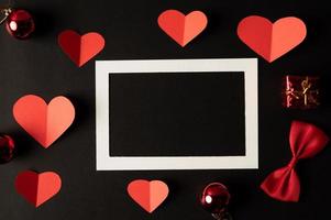 weißer Bilderrahmen und rotes Herzpapier auf schwarzem Hintergrund. foto