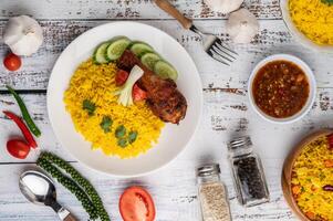 Chicken Biryani in einem Teller mit Gewürzen auf einem weißen Holzboden foto