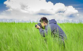 Mann nehmen Bild mit Kamera im das Feld, Fotograf im das Feld nehmen ein Bild, Latino Mann im ein Grün Feld nehmen ein Bild foto