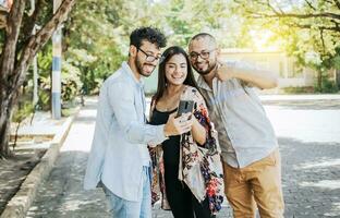 glücklich freunde Aufpassen ein Zelle Telefon im das Straße. drei glücklich freunde Teilen das Zelle Telefon im das Straße. Konzept von glücklich freunde Teilen Medien auf ein Telefon foto