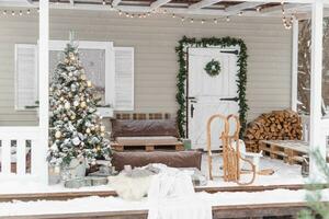 das Veranda von ein Land Haus dekoriert zum Weihnachten und Neu Jahr Feiertage. Weihnachten Baum auf das Veranda von das Haus im Winter. foto