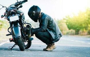 Biker reparieren Motorrad auf das Straße. Motorradfahrer Festsetzung das Motorrad auf das Straße, Mann Überprüfung seine Motorrad auf das Straße foto