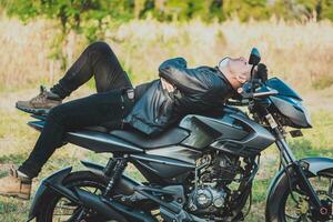 Motorradfahrer im Jacke Lügen auf seine Motorrad im das Landschaft. Biker Mann Lügen Nieder auf seine Motorrad draußen foto