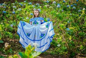 jung nicaraguanisch Frau im traditionell Volk Kostüm im ein Feld von MILFLORES, lächelnd Frau im National Volk Kostüm im ein Feld umgeben durch Blumen. nicaraguanisch National Volk Kostüm foto
