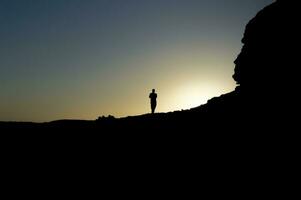 Bild von das Silhouette von ein Mann auf ein Felsen mit das Sonne hinterleuchtet, Silhouette von ein Person auf ein Felsen, Unternehmerschaft Konzept foto