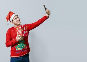 Weihnachten gut aussehend Mann nehmen ein Selfie halten ein Geschenk isoliert. glücklich Kerl nehmen ein Weihnachten Selfie isoliert, lächelnd jung Mann im Weihnachten Hut halten ein Geschenk und nehmen ein Selfie isoliert foto