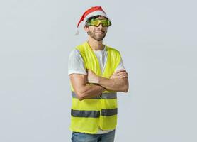Porträt von ein lächelnd Ingenieur im ein Weihnachten Hut, Porträt von ein Ingenieur im ein Weste und ein Weihnachten Hut. Porträt von heiter Ingenieur im Weste und Weihnachten Hut mit Waffen gekreuzt. foto