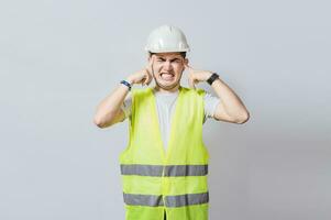 jung Ingenieur Abdeckung seine Ohren isoliert, Baumeister Mann mit Ohr Schmerz, Konzept von Ingenieur Abdeckung seine Ohren mit Schmerzen Ausdruck, Ingenieur mit Ohr Schmerzen isoliert foto