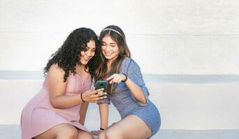 zwei Mädchen zeigen beim ihr Zelle Telefon, Mädchen zeigen ihr Smartphone zu ihr Freund, Mädchen Überprüfung ihr Zelle Telefon mit ihr Freund foto