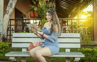 ein süß Mädchen Sitzung auf ein Bank lesen ein Buch, ziemlich jung Latein Mädchen lesen ein Buch auf ein Bank foto
