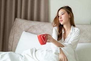 Porträt schöne Frau wacht auf und hält Kaffeetasse oder Tasse auf dem Bett foto