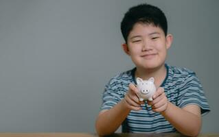 asiatisch Junge Speichern Geld setzt Münzen im Schweinchen Bank, speichern Geld und Finanzen Konzept, Speichern Geld zum das Zukunft foto