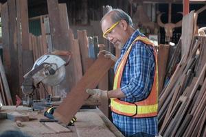 Senior asiatischer Tischler, der Holz in der Fabrik schneidet. foto