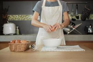 Köchin in einer weißen Schürze knackt ein Ei in der heimischen Küche.