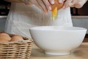 Köchin in einer weißen Schürze knackt ein Ei in der heimischen Küche.
