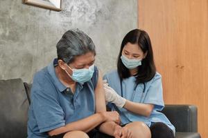 Eine asiatische Ärztin impft zu Hause einen älteren Mann.
