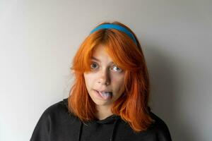 komisch Teen Mädchen mit rot Haar zeigt an Blau Zunge. das Mädchen ist täuschen um foto