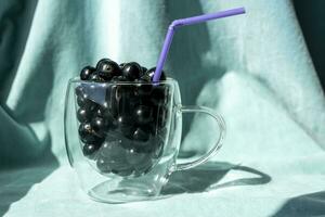 Sommer- frisch schwarz Johannisbeere Beeren im ein Glas Becher mit ein Cocktail Tube foto