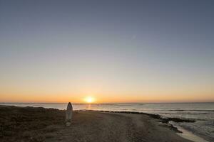 Windsurfen Tafel Stapeln im das Sand von das Strand und ein warm Sonnenaufgang beim das horzion foto