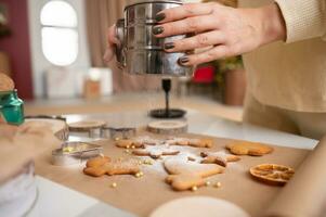 ein Frau Hände streuen Ingwer Kekse mit pulverisiert Zucker foto