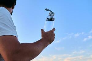 ein Mann hält ein Flasche von Wasser gegen das Hintergrund von ein See. foto