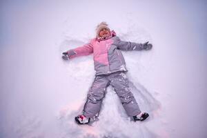 ein Mädchen macht ein Schnee Engel im Weiß Schnee im Winter. foto