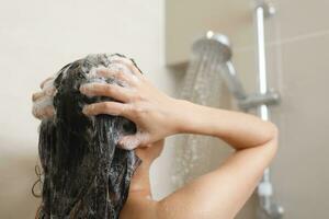 Frau nehmen Dusche und Waschen Haar mit Shampoo foto