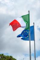 Flaggen der italienischen und europäischen Union wehen gegen einen bewölkten Himmel foto