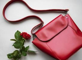 rote Lederfrauentasche und Rose auf grauem Hintergrund foto