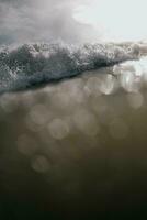 ein Welle geht kaputt auf das Strand mit ein Sonne leuchtenden durch das Wasser foto