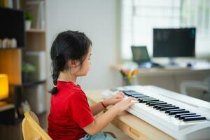 glücklich wenig asiatisch süß Baby Mädchen Lächeln spielen Lernen online Klavier Musik- im Leben Zimmer beim heim. das Idee von Aktivitäten zum Kind beim Zuhause während Quarantäne. Musik- Lernen lernen. foto