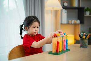 jung süß asiatisch Baby Mädchen tragen rot T-Shirt ist Lernen das Abakus mit farbig Perlen zu lernen Wie zu Anzahl auf das Tabelle im das Leben Zimmer beim heim. Kind Baby Mädchen Entwicklung studieren Konzept. foto