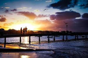 Sonnenuntergang am Pier, blaue und goldene Farben, Menschen und Möwen foto