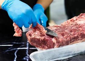 Koch schneidet rohes Fleisch mit einem Messer auf einem Brett, Koch schneidet rohes Fleisch foto