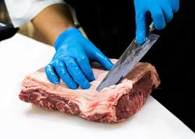 Koch schneidet rohes Fleisch mit einem Messer auf einem Brett, Koch schneidet rohes Fleisch