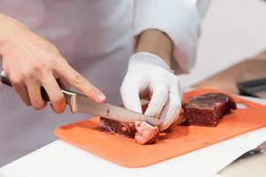 Koch schneidet frisches rohes Fleisch mit Messer in der Küche