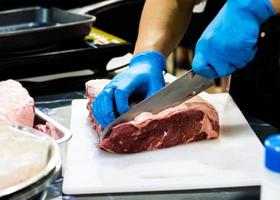 Koch schneidet rohes Fleisch mit einem Messer auf einem Brett, Koch schneidet rohes Fleisch
