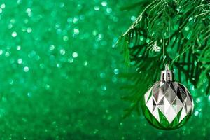 silberne Weihnachtskugel auf glänzendem grünem Hintergrund. Neujahrskonzept
