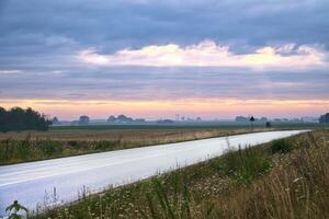 Land Straße mit Kurve führt durch landwirtschaftlich Felder. schwer Wolken im das Himmel foto