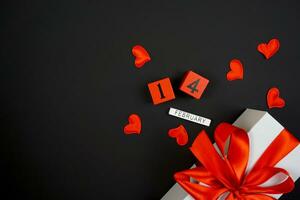 auf ein schwarz Hintergrund ist ein Valentinstag Tag Geschenk, Engagement Ringe und ein Inschrift auf Februar 14 foto