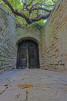 Aussicht von ein hölzern braun Tor im ein historisch bewachsen natürlich Stein Mauer von das Boden foto
